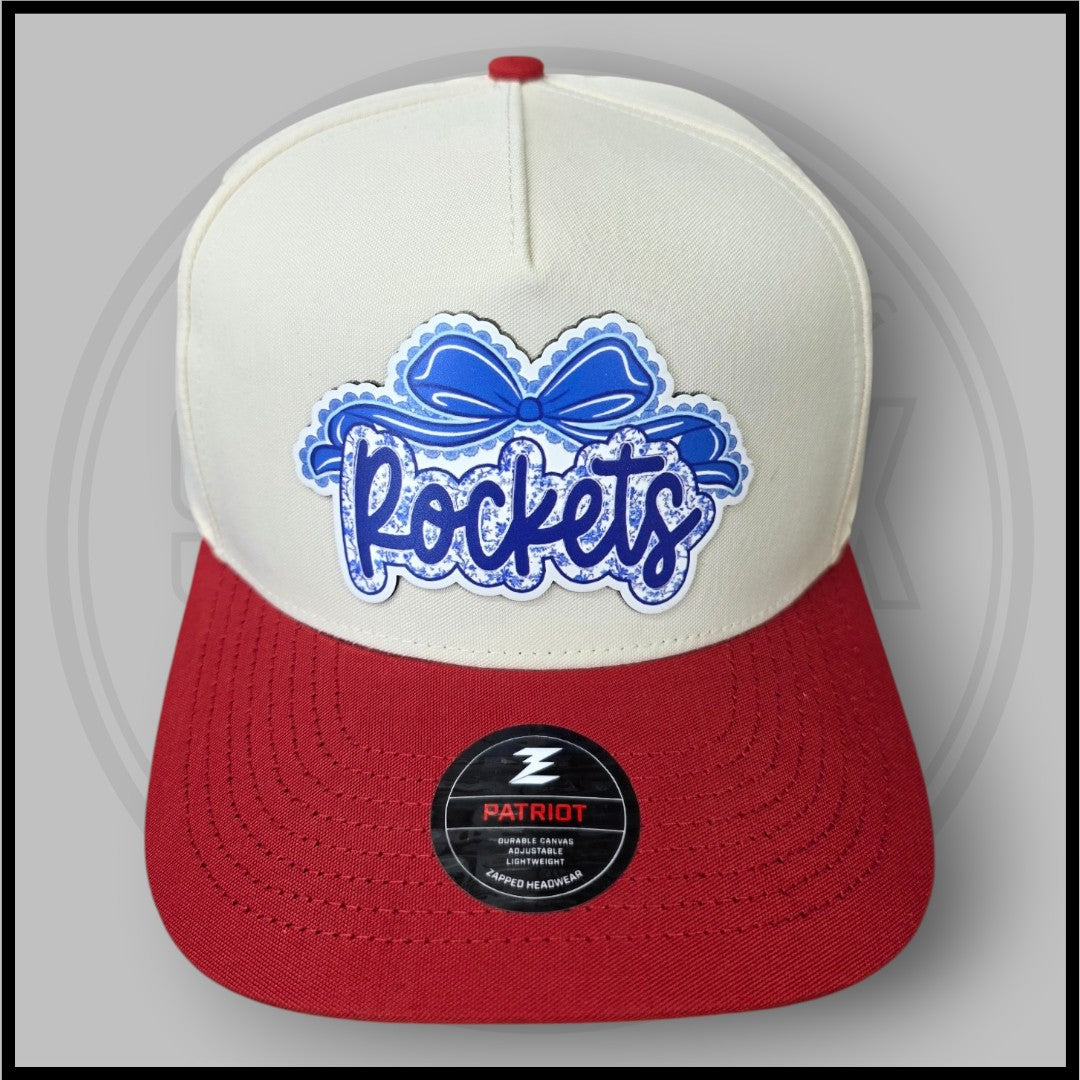 Cream and red baseball cap with large blue script logo patch and Patriot badge