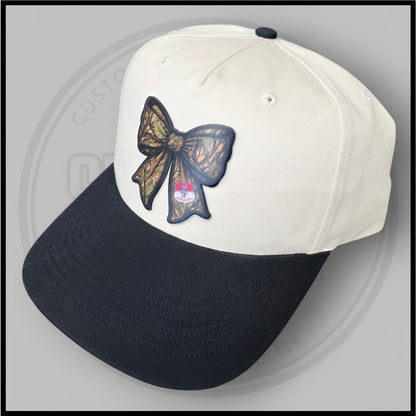 Two-tone baseball cap with cream crown, black brim, and large bow applique on side