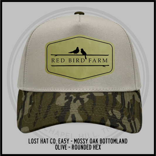 Rounded hex baseball cap with tan crown, olive bottomland camo brim, front patch with bird logo