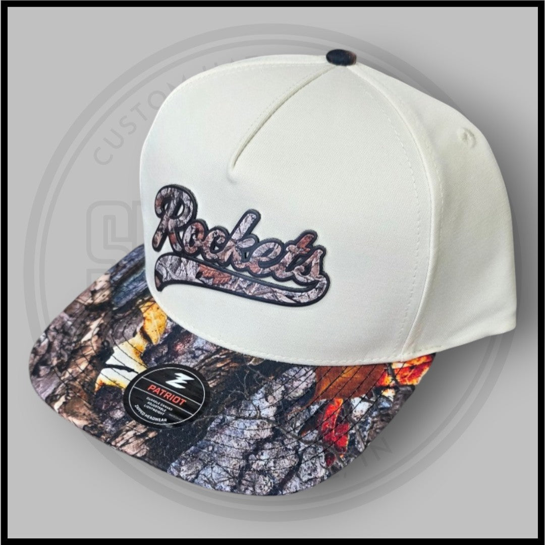 Cream baseball cap with Rockets logo embroidery and Patriot patch on camo brim