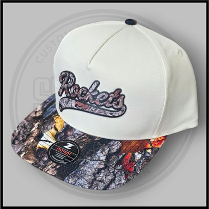 Cream baseball cap with Rockets logo embroidery and Patriot patch on camo brim